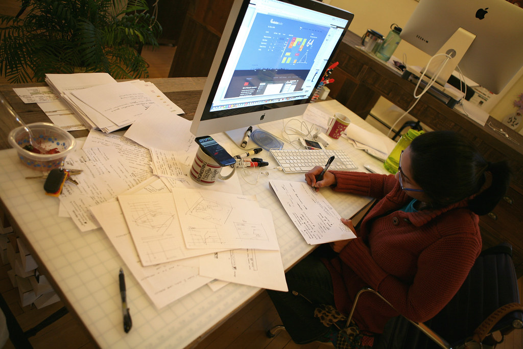 Designer sketching interface concepts beside a large desktop monitor